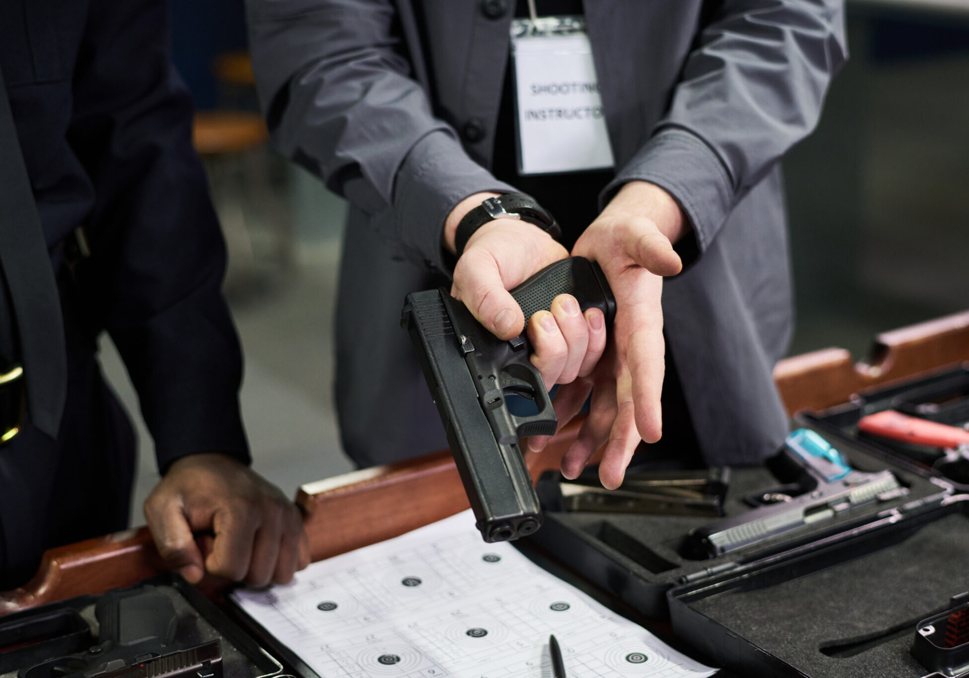 Close-up shot showing instructor guiding individual on proper handgun handling technique during firearm safety training in an indoor range environment